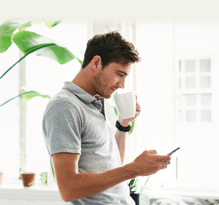 Un hombre bebe café mientras sostiene un teléfono móvil