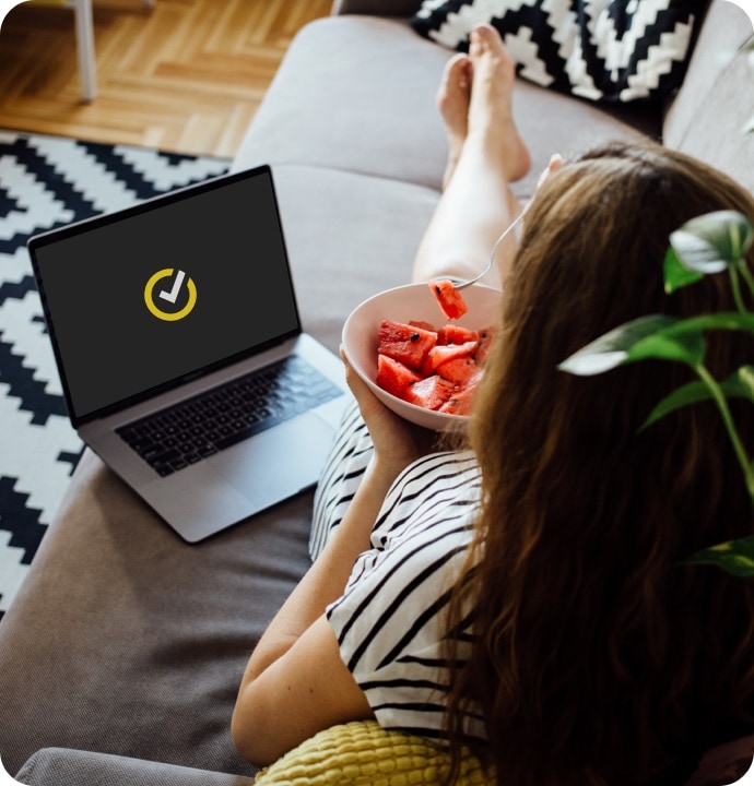 Mujer comiendo fruta con una computadora portátil a su lado que muestra el símbolo de NortonLifeLock.