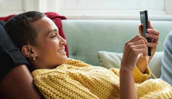 Una mujer en un sofá está mirando un celular mientras ejecuta Norton 360 con AntiVirus Plus.