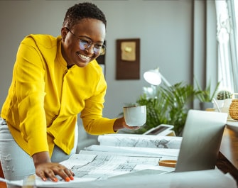 Mujer sonriente con una taza en la mano mirando una computadora portátil